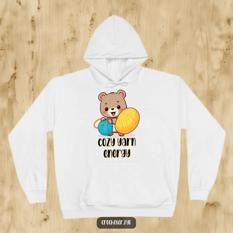 Funny hoodie showcasing a delighted bear character diligently winding a massive ball of vibrant yarn, embodying creative passion.