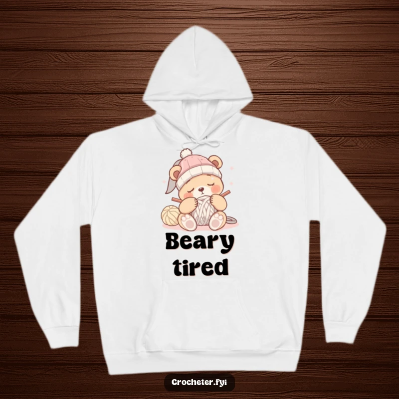 Funny sleepy bear hoodie showing a bear attempting to crochet a hat while clearly dozing off, emphasizing comfort.